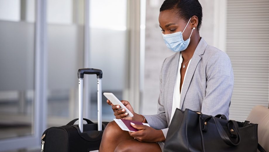 Business woman in airport with face mask checking phone
