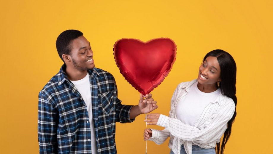 Anniversary, valentines day and romantic gift. Happy african american guy and lady look at each other through balloon
